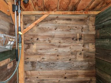 A wooden shower with metal showerhead and hose mounted on the wall at Harri's Hut in Bishop's Lydeard