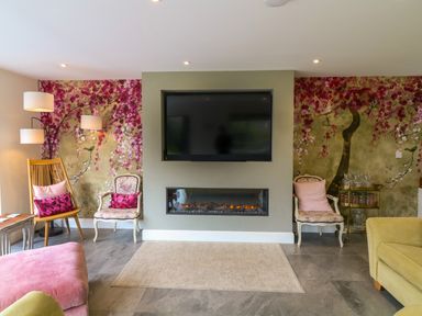 A living room with a wall mounted TV above a fireplace and floral wallpaper at Channel View House in Wadebridge