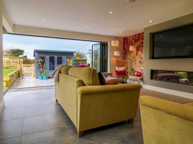 A living room with sofas a wall-mounted TV a modern fireplace and a garden shed outside at Channel View House in Wadebridge