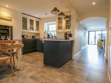 A kitchen with a black island and hanging lights next to a dining table and chairs at Channel View House in Wadebridge