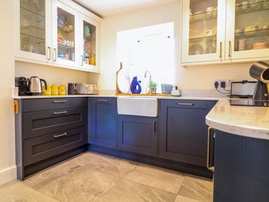 A kitchen with blue lower cabinets white upper cabinets and a white farmhouse sink at Channel View House in Wadebridge