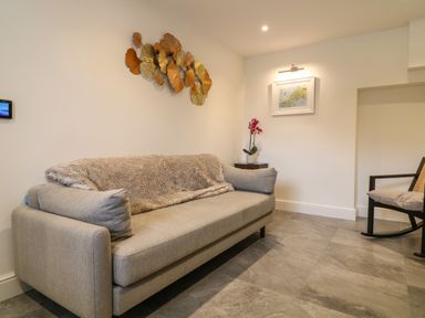 A room with a grey sofa covered with a blanket a small side table with a flower pot and a framed picture on the wall at Channel View House in Wadebridge