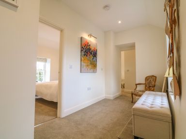 A hallway with carpeted floor a painting on the wall an upholstered bench an armchair and doors leading to other rooms at Channel View House in Wadebridge