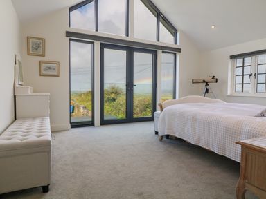 A bedroom with a bed a telescope and large windows overlooking greenery at Channel View House in Wadebridge