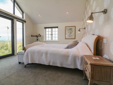 A bedroom with a double bed bedside table telescope and large windows at Channel View House in Wadebridge