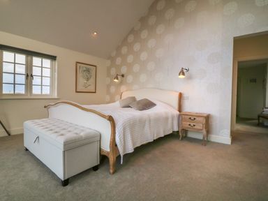 A bedroom with a bed a bench at the foot of the bed a wooden nightstand with drawers and a window at Channel View House in Wadebridge