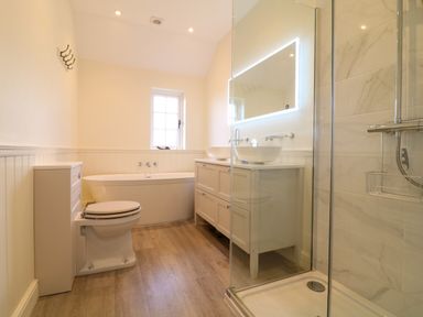 A bathroom with a toilet bathtub double sinks shower and a window at Channel View House in Wadebridge