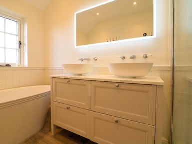 A bathroom with two above-counter sinks on a vanity unit and a freestanding bathtub by a window at Channel View House in Wadebridge
