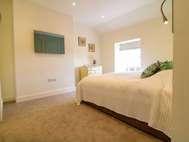 A bedroom with a bed covered in white bedding a chest of drawers and a wall mounted television at Channel View House in Wadebridge