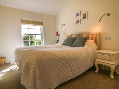 A bedroom with a bed with two pillows bedside table a window with a blind and three framed pictures on the wall at Channel View House in Wadebridge