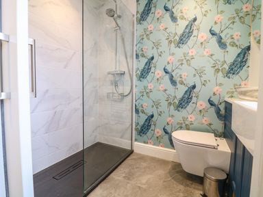 A bathroom with a walk-in shower, toilet, and peacock patterned wallpaper at Channel View House in Wadebridge