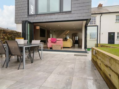 A patio with outdoor dining table and chairs leading to a living room with sofas at Channel View House in Wadebridge