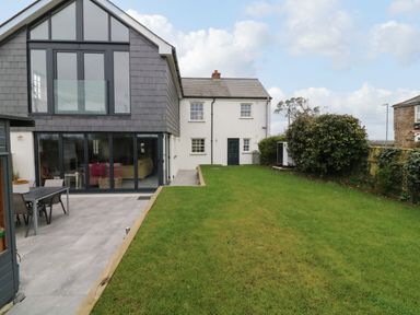 A backyard with grass lawn and a paved patio area next to a modern two-story house at Channel View House in Wadebridge