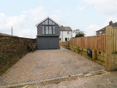 A gravel driveway between a stone wall and a wooden fence leading to a two-story building at Channel View House in Wadebridge