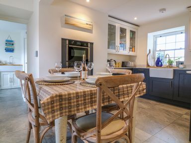 A kitchen with a dining table set with plates and wine glasses and wooden chairs at Channel View House Wadebridge