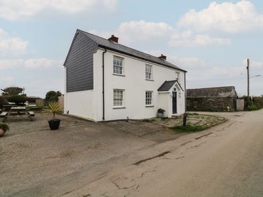 A two-story white house with slate roof and a side garden with a picnic table and potted plants at Channel View House in Wadebridge
