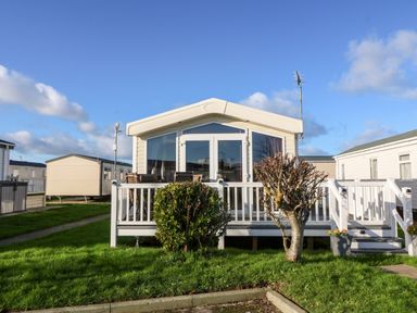 A mobile home with a white deck and patio furniture in front of a grassy area at Snape Lodge in Towyn