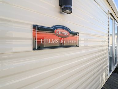 Exterior of a mobile home with a sign that reads Helmsley Lodge near a glass door at Snape Lodge in Towyn