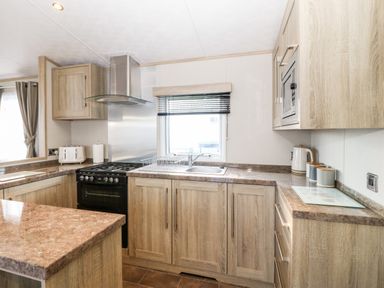 A kitchen with wooden cabinets a countertop a sink a stove a microwave a toaster and a kettle at Snape Lodge in Towyn