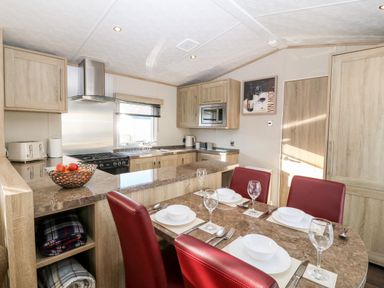 A kitchen and dining area with red chairs and table set with plates and glasses at Snape Lodge in Towyn