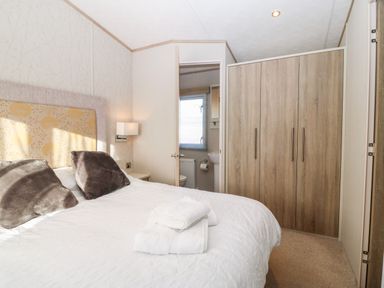 A bedroom with a bed with pillows and folded towels a wardrobe and a door leading to an en suite bathroom at Snape Lodge in Towyn