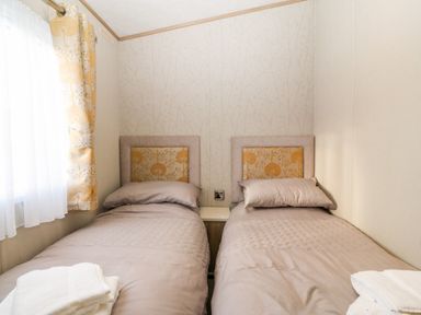 A bedroom with two single beds side by side and a window with patterned curtains at Snape Lodge in Towyn