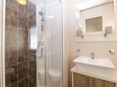 A bathroom with a shower enclosure and a sink with a mirror above at Snape Lodge in Towyn