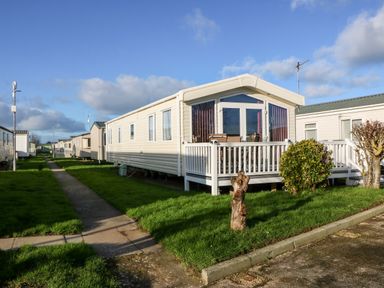 A row of mobile homes with green lawns and a paved walkway at Snape Lodge in Towyn
