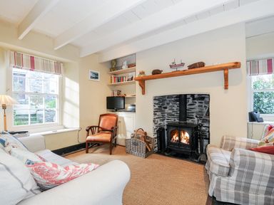A living room with a sofa armchair wood burning stove and bookshelf at Lowen Cottage in Boscastle