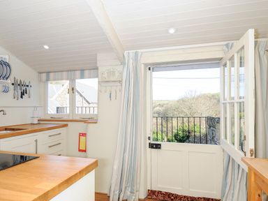 A kitchen with wooden countertops knives on the wall a half glass door open to a garden at Lowen Cottage in Boscastle