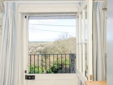 An open white door with a black metal railing outside showing trees and hills at Lowen Cottage in Boscastle