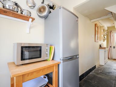 A kitchen area with a microwave on a wooden table and a silver fridge in a hallway at Lowen Cottage in Boscastle