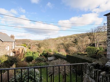 A garden with bushes and trees overlooking a countryside landscape with houses at Lowen Cottage in Boscastle