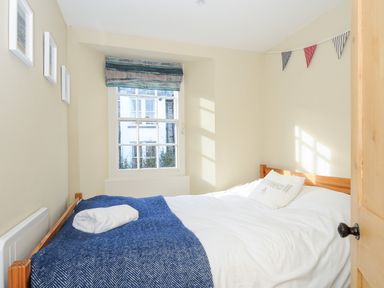 A bedroom with a wooden bed a blue blanket white pillow a window with a blind and wall decorations at Lowen Cottage in Boscastle