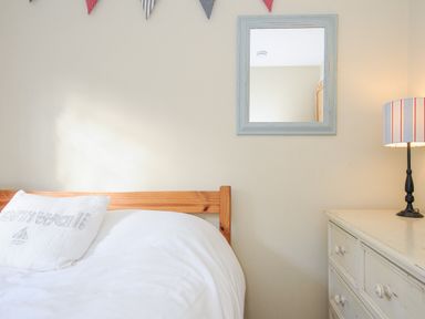 A bedroom with a wooden bed frame white pillow and bedding a mirror white dresser and a lamp at Lowen Cottage in Boscastle