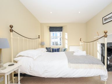 A bedroom with a bed with white linens and a gray blanket next to a window with cushions at Lowen Cottage in Boscastle