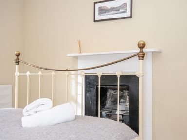 A bed with a metal frame and two rolled towels on it in front of a fireplace with a painting above at Lowen Cottage in Boscastle