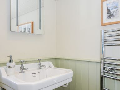 A bathroom sink with two taps a soap dispenser a mirror above and a towel radiator on the wall at Lowen Cottage in Boscastle