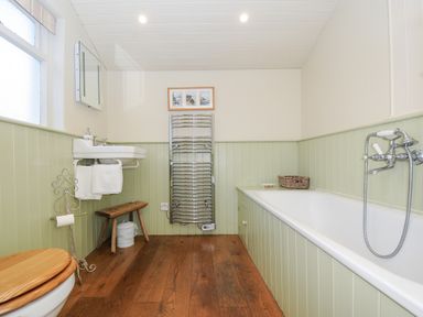 A bathroom with a bathtub sink toilet wooden bench and towel heater at Lowen Cottage in Boscastle