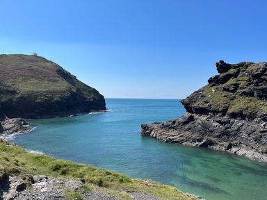 Rocky coastline with grassy cliffs and blue ocean under clear sky at Lowen Cottage in Boscastle