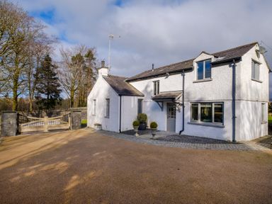 A white two-story house with a gated driveway and trees in the background at Gate House in Killington near Sedbergh