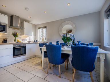 A kitchen and dining area with white cabinets blue chairs and a table with flowers at Gate House in Killington near Sedbergh