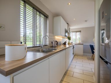 A kitchen with white cabinets a wooden countertop a sink and a window with blinds at Gate House Killington near Sedbergh