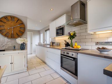 A kitchen with white cabinets wooden countertops a large wall clock flowers and kitchen appliances at Gate House Killington near Sedbergh