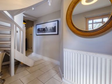 A hallway with white stairs a radiator a round mirror and a black and white framed picture at Gate House in Killington near Sedbergh