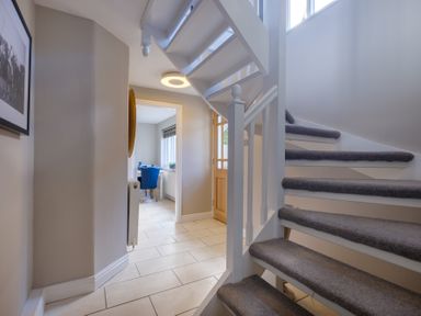 A hallway with a staircase and a view into a room with a blue chair at Gate House in Killington near Sedbergh