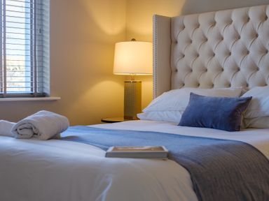 A bedroom with a bed with a tufted headboard a folded towel a lamp and a window at Gate House Killington near Sedbergh