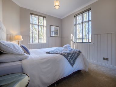 A bedroom with a bed white bedding a bedside lamp two windows and folded towels on the bed at Gate House in Killington near Sedbergh