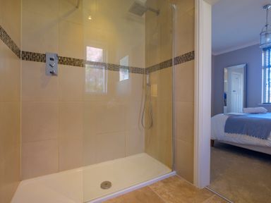 A tiled walk in shower with a glass door and a view into a bedroom with a bed and mirror at Gate House in Killington near Sedbergh