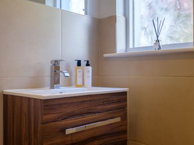 A bathroom sink with a faucet two soap dispensers and a window with scented sticks on the sill at Gate House in Killington near Sedbergh